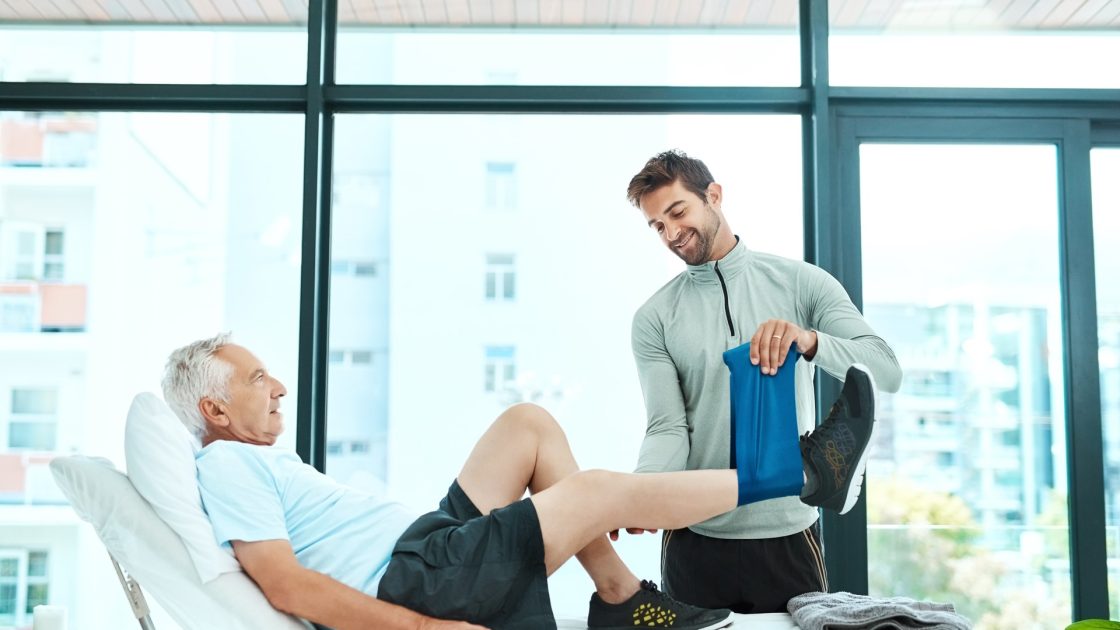 Physiotherapist assisting an older patient with a guided leg exercise during hip replacement rehab at Rehab Genius Bolton