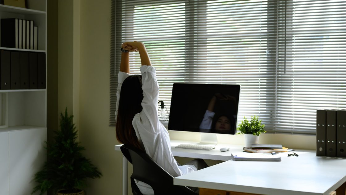 Employee stretching at a home office desk, representing workplace physiotherapy support from Rehab Genius Health Preston